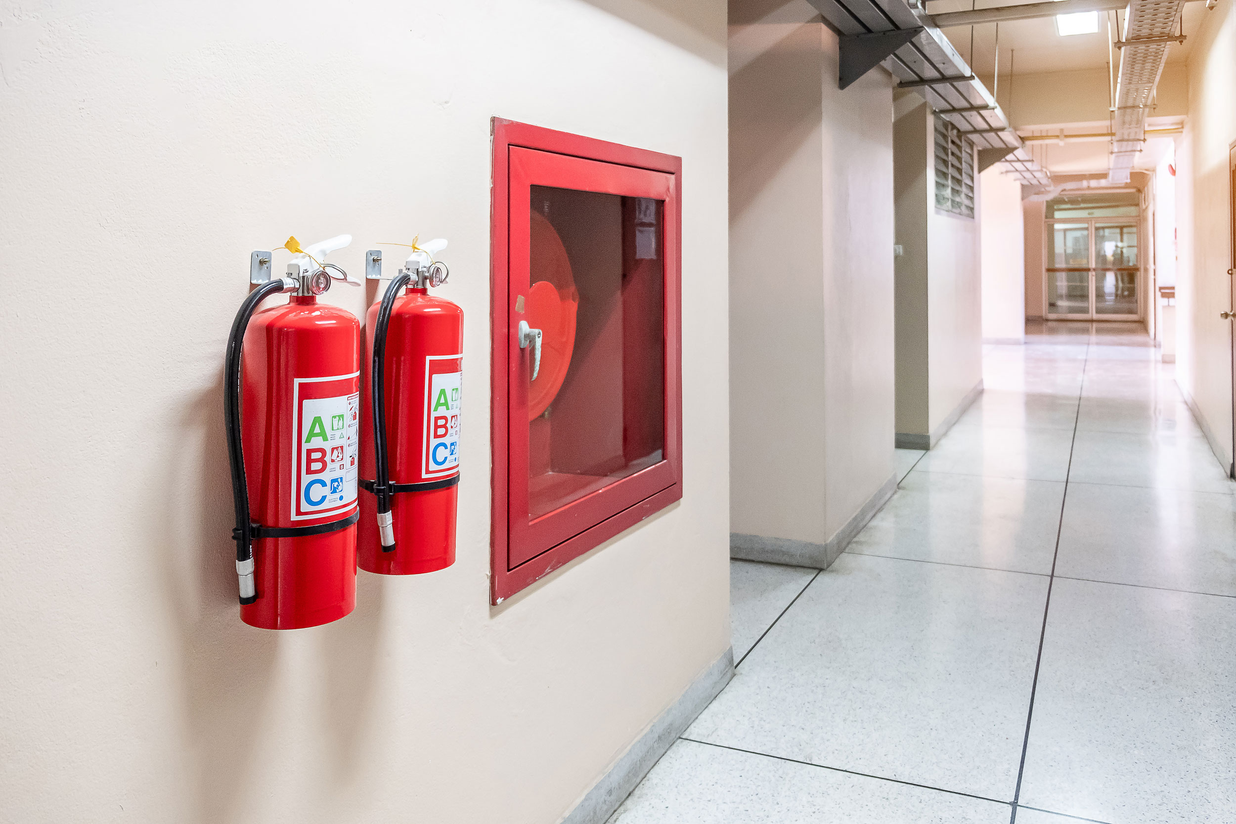 ABC fire extinguishers mounted beside a fire hose cabinet in a commercial building in Southeast Missouri